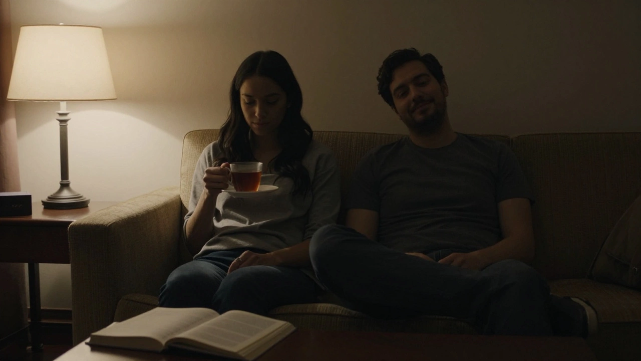 Two people sitting comfortably on a sofa in a hotel room, softly lit by a bedside lamp, sharing quiet moments.